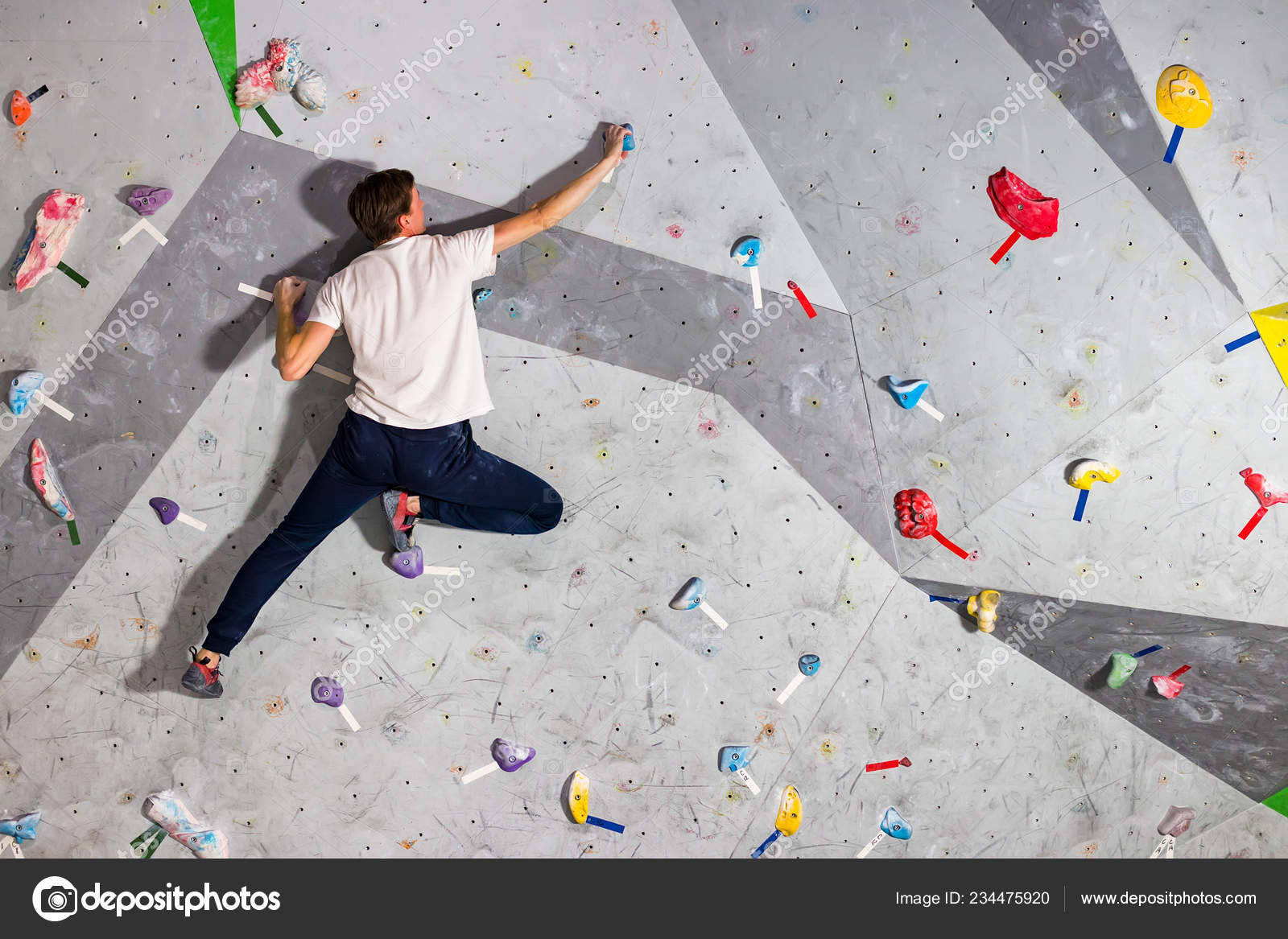 Rock climber man hanging on a bouldering climbing wall, inside on