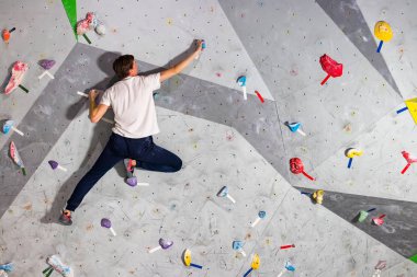Rock climber erkeği bouldering tırmanma duvarı üzerinde içinde renkli kanca asılı