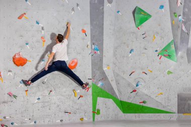 Climber erkeği bir tırmanma duvarı bouldering duvar üzerinde bir sicim içinde renkli kanca asılı