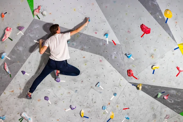 Skalní muž horolezec visí na bouldering horolezeckou stěnu, na barevné háčky — Stock fotografie