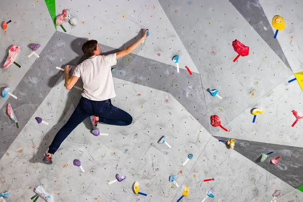 Rock climber erkeği bouldering tırmanma duvarı üzerinde içinde renkli kanca asılı