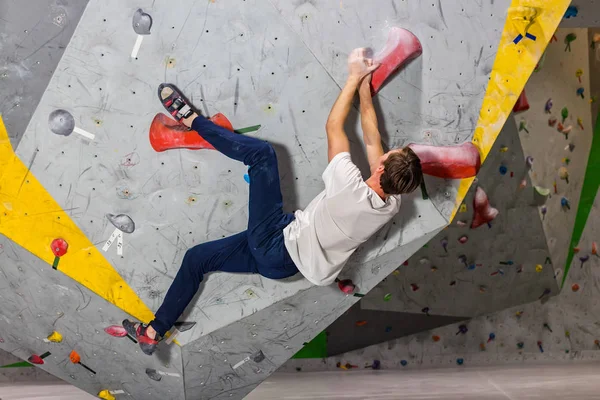 Hombre escalador colgando en una pared de escalada de cantos rodados, en el interior de ganchos de colores —  Fotos de Stock