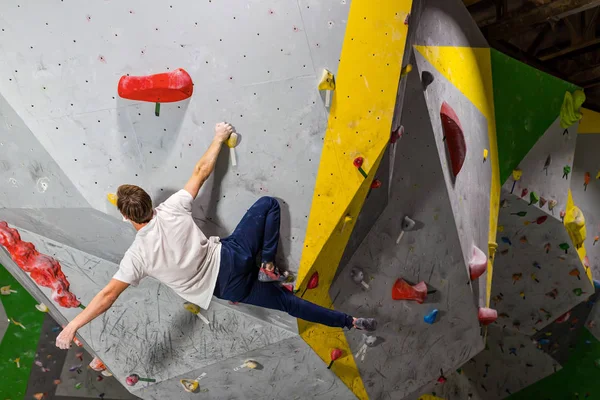Rock climber erkeği bouldering tırmanma duvarı üzerinde içinde renkli kanca asılı — Stok fotoğraf