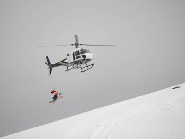 Skier freerider jumps from helicopter heliski on a snowy mountain clipart
