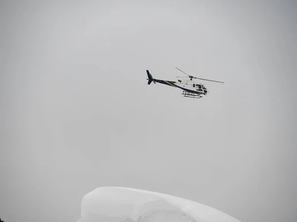 Vit helikopter flyger över snötäckta berg på en molnig dag — Stockfoto