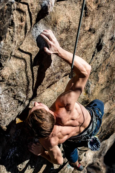 裸の胴を持つ男性登山家が保険金を持って岩の上に登り — ストック写真
