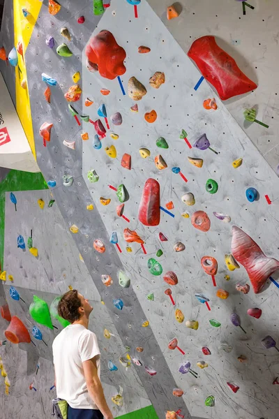 Escalador de roca se para y mira a la pared de escalada con ganchos en la sala de rocas —  Fotos de Stock