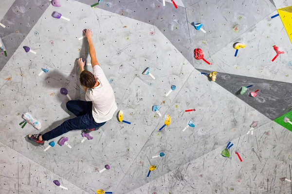 Rock climber erkeği bouldering tırmanma duvarı üzerinde içinde renkli kanca asılı — Stok fotoğraf