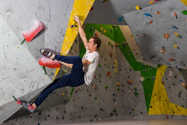Homem alpinista pendurado em uma parede de escalada, dentro de ganchos coloridos — Fotografia de Stock
