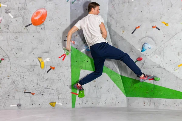 Skalní muž horolezec visí na bouldering horolezeckou stěnu, na barevné háčky — Stock fotografie