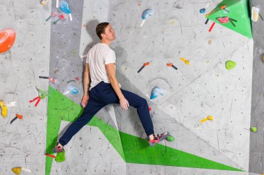 Rock climber erkeği bouldering tırmanma duvarı üzerinde içinde renkli kanca asılı