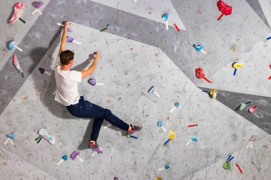 Rock climber erkeği bouldering tırmanma duvarı üzerinde içinde renkli kanca asılı