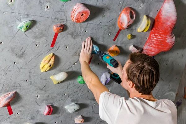 Rock klimmer vastmaakt de haak met een schroevendraaier bij de klimmuur in de hal van boulder — Stockfoto