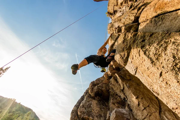 Climber Extreme climbs a rock on a rope with the top insurance, against the blue sky, bottom view — Stock Photo, Image