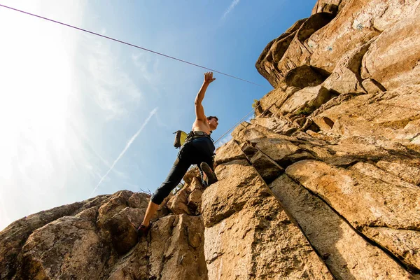 Climber Extreme climbs a rock on a rope with the top insurance, against the blue sky, bottom view — Stock Photo, Image