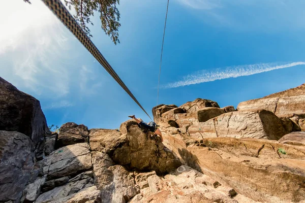 Ακραία ορειβάτης ανεβαίνει ένα βράχο σε ένα σχοινί με την κορυφή, τις ασφαλίσεις το γαλάζιο του ουρανού, κάτω όψη — Φωτογραφία Αρχείου