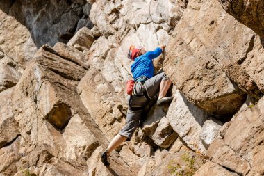 Renkli elbise daha düşük sigorta erkeklerde ve sonbaharda bir şapka ile kayaya kız kaya tırmanışçısı tırmanıyor