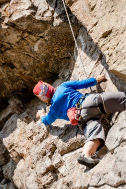 Renkli elbise daha düşük sigorta erkeklerde ve sonbaharda bir şapka ile kayaya kız kaya tırmanışçısı tırmanıyor