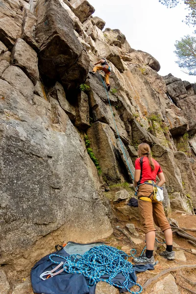Ένας ορειβάτης άνθρωπος πάνω σε ένα βράχο με χαμηλότερη ασφαλιστική ασφαλίζει τα κορίτσι ορειβάτης — Φωτογραφία Αρχείου