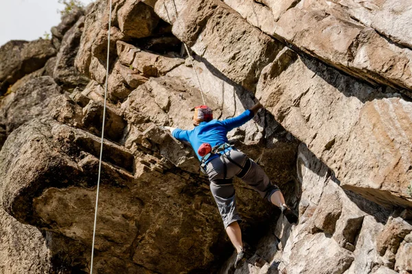 Κορίτσι ροκ ορειβάτης ανεβαίνει πάνω στο βράχο με χαμηλότερη ασφαλιστική ανδρών με πολύχρωμα ρούχα και καπέλο το φθινόπωρο — Φωτογραφία Αρχείου