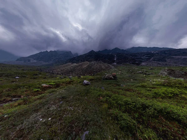 Black mountains in rain clouds, the foot covered with stones and green grass. Wide angle panorama