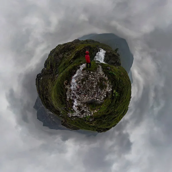 Man in red stands under waterfall on black rock in mountains on cloudy rainy day.. . Tiny little planet 360 — Stock Photo, Image