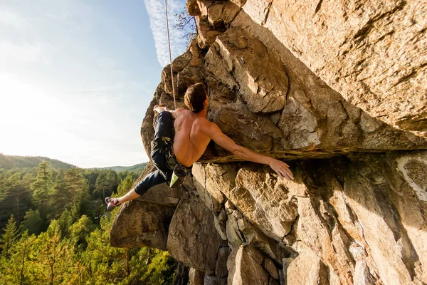 Ακραία ορειβάτης ανεβαίνει ένα βράχο σε ένα σχοινί με την κορυφαία ασφαλιστική, με θέα στο δάσος — Φωτογραφία Αρχείου