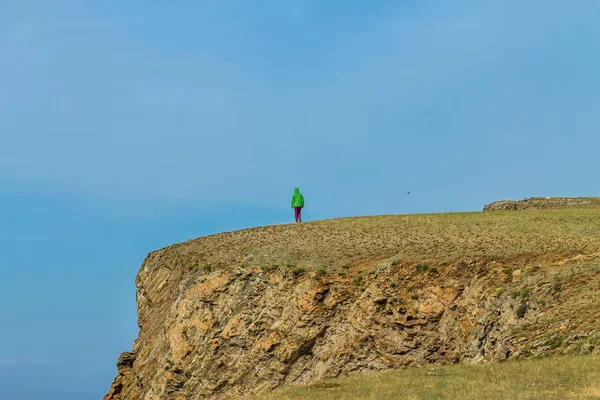 adam mavi gökyüzüne karşı yüksek kayalık bir burun üzerinde duruyor