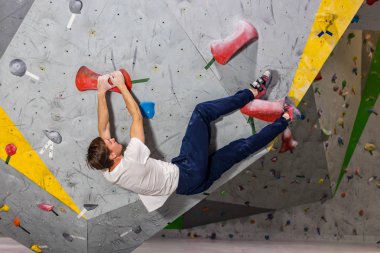 Rock climber erkeği bouldering tırmanma duvarı üzerinde içinde renkli kanca asılı