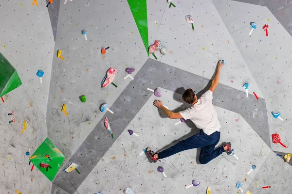 Bergsteiger Mann hängt an einer Boulderkletterwand, innen an farbigen Haken — Stockfoto