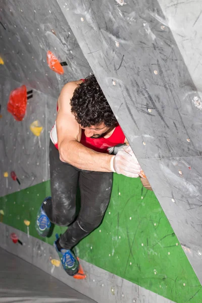 Skalní muž horolezec visí na bouldering horolezeckou stěnu, na barevné háčky — Stock fotografie