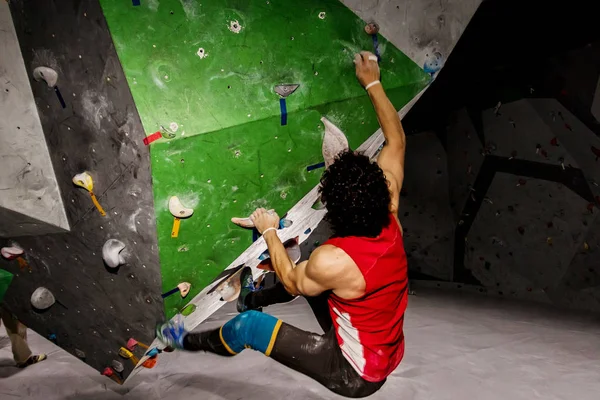 Hombre escalador colgando en una pared de escalada de cantos rodados, en el interior de ganchos de colores —  Fotos de Stock