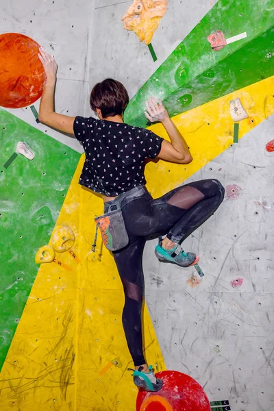 Скалолазательница, висящая на валунной стене, внутри на цветных крючках — стоковое фото