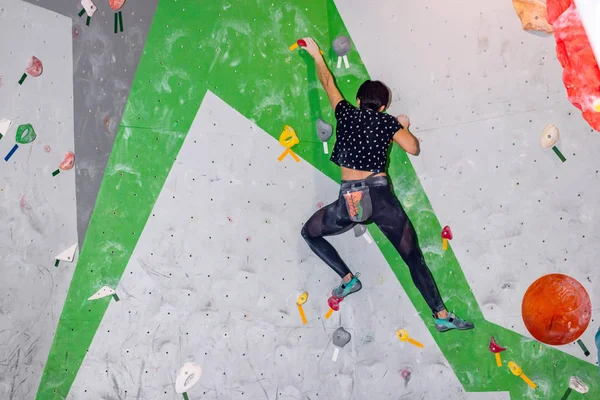 攀岩的女人挂在一个巨大的攀岩墙上，里面挂着彩色的钩子 — 图库照片