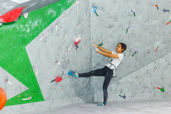 Mulher alpinista pendurada em uma parede de escalada, dentro de ganchos coloridos — Fotografia de Stock