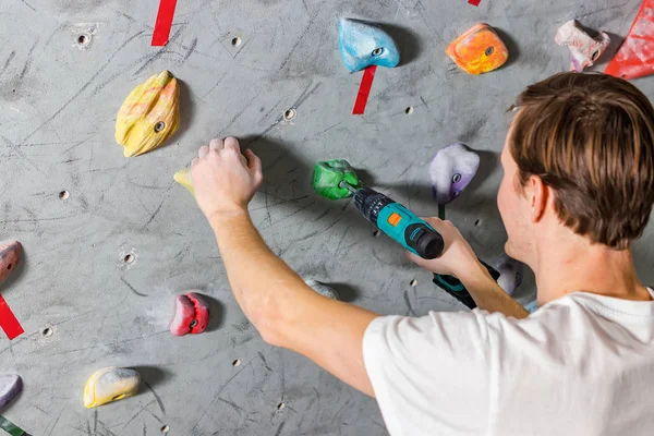 Rock climber fastens the hook with a screwdriver at the climbing wall in the boulder hall — Stock Photo, Image