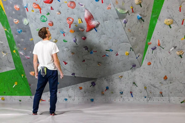 Alpinista de rocha fica e olha para a parede de escalada com ganchos no salão de pedras — Fotografia de Stock