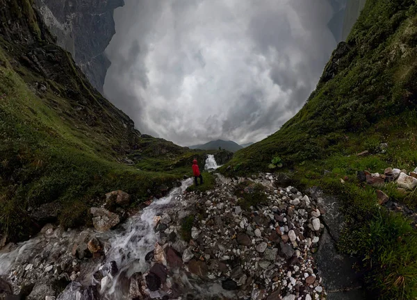 Kırmızılı adam dağlarda siyah kaya şelale altında bulutlu yağmurlu günde duruyor... Geniş panorama — Stok fotoğraf