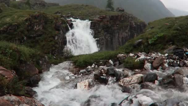 Cascata che scorre tra le montagne di rocce ed erba verde dell'Islanda paesaggio nebbioso — Video Stock