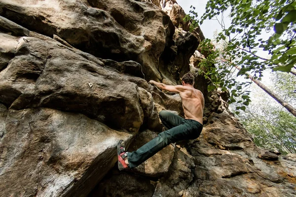 Rots klimmer klimt boulderen op een klif op bos. Lage hoek van sterke rotsklimmen man opknoping vrij op rots met sunflare — Stockfoto