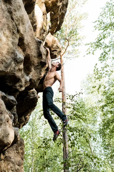 Rots klimmer klimt boulderen op een klif op bos. Lage hoek van sterke rotsklimmen man opknoping vrij op rots met sunflare — Stockfoto