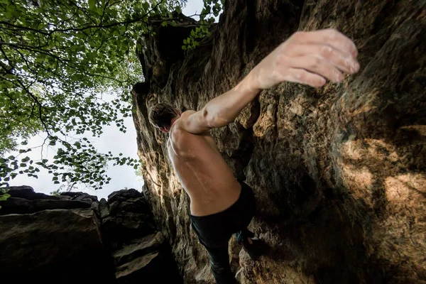 Rots klimmer klimt boulderen op een klif op bos. Lage hoek van sterke rotsklimmen man opknoping vrij op rots met sunflare — Stockfoto