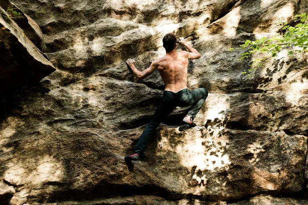 Rots klimmer klimt boulderen op een klif op bos. Lage hoek van sterke rotsklimmen man opknoping vrij op rots met sunflare — Stockfoto