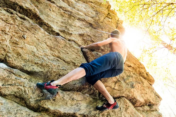Rock climber climbs bouldering on a cliff on forest. Low angle of strong rock climbing man hanging free on rock with sunflare — Stock Photo, Image