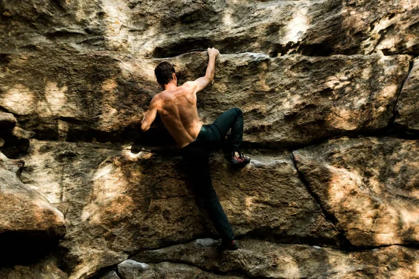 Rots klimmer klimt boulderen op een klif op bos. Lage hoek van sterke rotsklimmen man opknoping vrij op rots met sunflare — Stockfoto