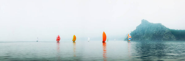 Регата яхт с апельсиновым парусом в туманное утро плавает по морю
