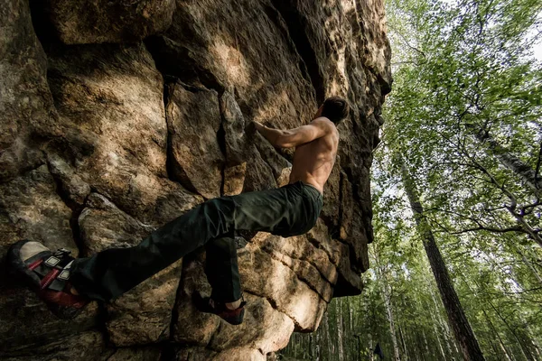 Rots klimmer klimt boulderen op een klif op bos. Lage hoek van sterke rotsklimmen man opknoping vrij op rots met sunflare — Stockfoto