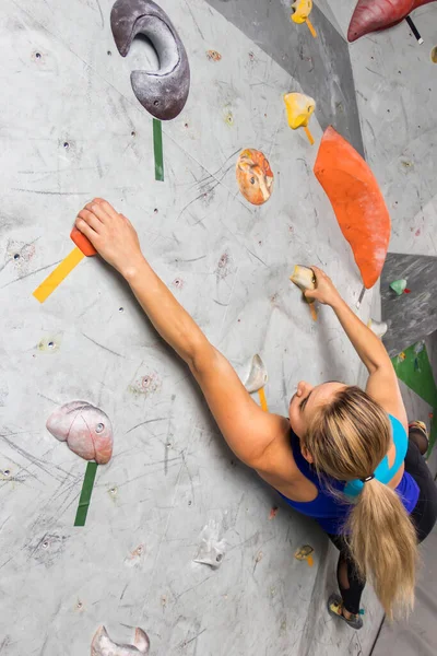 Kaya tırmanışçısı kadın kaya duvarında asılı, içinde renkli kancalar var. — Stok fotoğraf