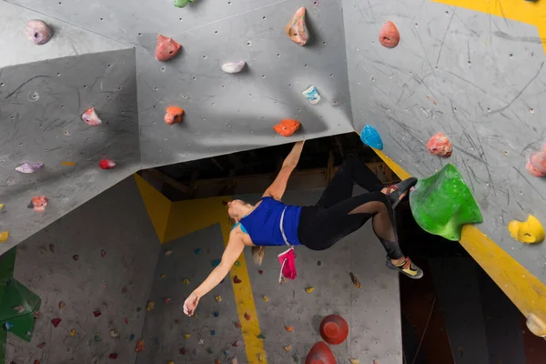 攀岩的女人挂在一个巨大的攀岩墙上，里面挂着彩色的钩子 — 图库照片