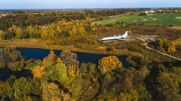 Vista aérea del avión en el bosque otoñal cerca del lago y hermoso paisaje. Hermoso paisaje de otoño con un avión . — Foto de Stock